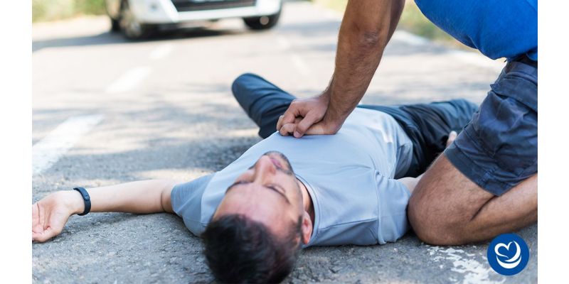 Caucasian man performing CPR on an unconscious man in the road.