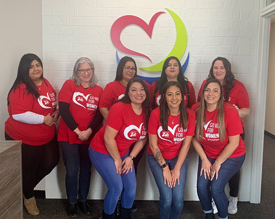 Group of female WorldPoint employees wearing red in front of the WorldPoint logo for Go Red for Women Day