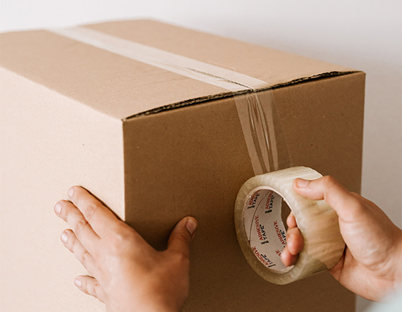 Hands applying packing tape to cardboard shipping box