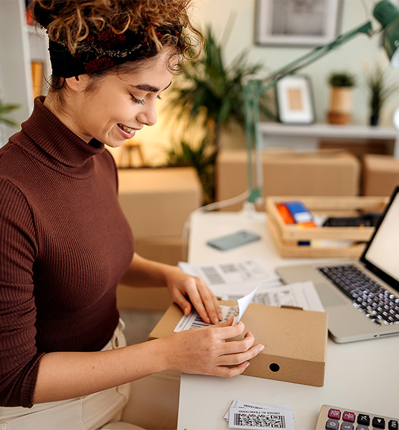 Woman seated at laptop applying shipping label to box