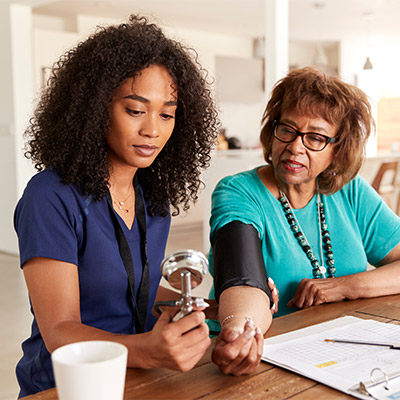 Black female nurse takes blood pressure measurement of elderly African American woman in her home
